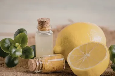 Połówka i cała cytryna obok małych buteleczek z olejkiem i solą kąpielową oraz zielonych liści