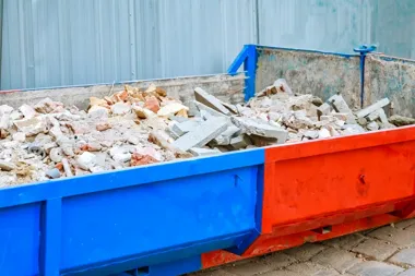 Niebiesko-czerwony kontener wypełniony gruzem budowlanym i resztkami betonu.