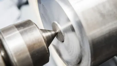 Zbliżenie wiertła obrabiającego metalowy cylinder na tokarce