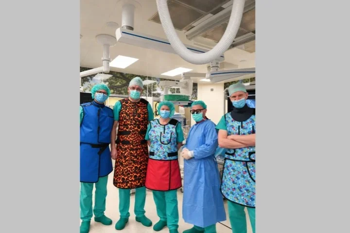 Pięcioro personelu medycznego w fartuchach ochronnych, czepkach i maskach stoi w sali operacyjnej.