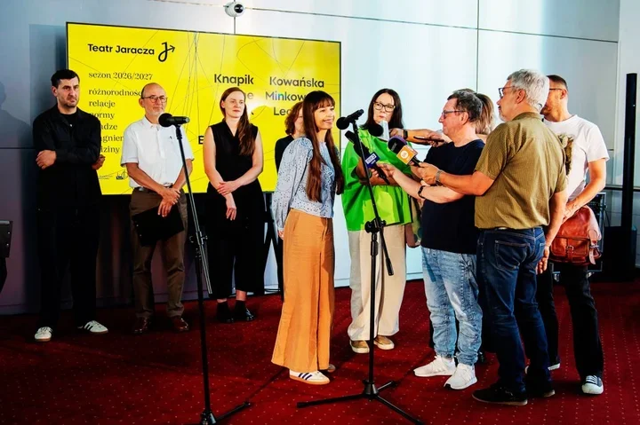 Grupa osób stoi na czerwonym dywanie przed żółtą ścianką Teatru Jaracza podczas konferencji prasowej sezonu 2026/2027.