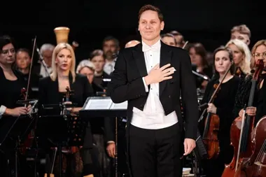 Dyrygent w białej muszce i fraku kłania się przed orkiestrą symfoniczną.