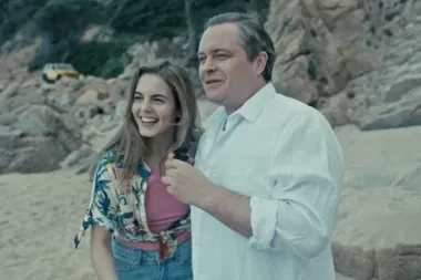 Mężczyzna w białej koszuli i kobieta w kolorowej koszuli stoją na skalistej plaży, kobieta się śmieje.