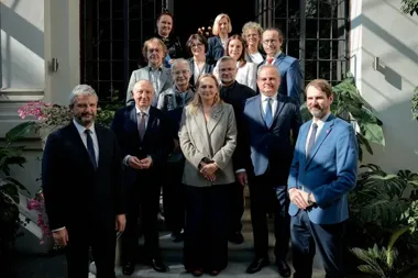Grupa osób, głównie w eleganckich garniturach, pozuje do pamiątkowego zdjęcia na schodach przed wejściem do budynku.