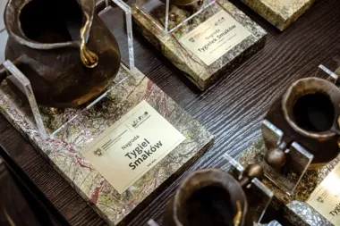 Nagrody "Tygiel Smaków" w postaci miedzianych tygielków na marmurowych postumentach leżą na ciemnym drewnianym stole.