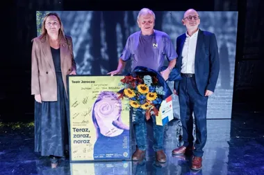 Trzy osoby stoją na scenie obok podpisanej plakaty Teatru Jaracza i bukietu kwiatów.