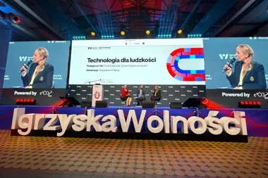 Panel dyskusyjny podczas wydarzenia Igrzyska Wolności na dużej scenie z ekranami i napisem w pierwszym planie.