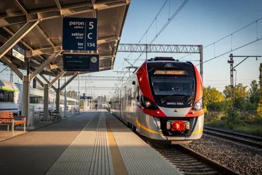 Nowoczesny pociąg pasażerski stoi przy peronie 5 na dworcu kolejowym w słoneczny dzień.